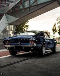 an old muscle car is parked on the side of the road in front of a modern building