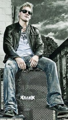 a man sitting on top of two amps in front of a brick wall and building