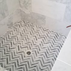 a white and gray bathroom with herringbone pattern on the floor, shower stall door open