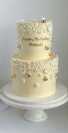 a three tiered cake decorated with daisies and bees