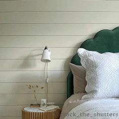 a bed with white sheets and pillows next to a green headboard on the wall