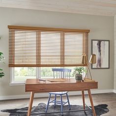 a wooden desk sitting under a window next to a chair and potted plant on top of a rug