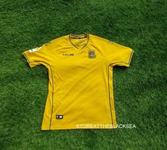 a yellow soccer jersey laying on the ground with green grass in the foreground and white lettering reading cleme