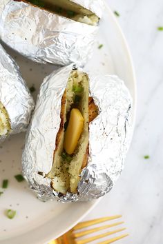 some food is wrapped in tin foil on a white plate with a fork and knife