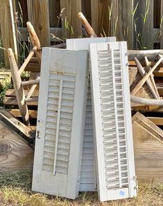 two old shutters leaning against each other on the ground in front of a fence