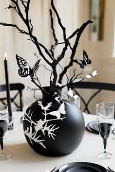 a black vase filled with butterflies on top of a white table cloth next to a candle