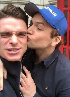 two men are kissing each other in front of a red phone booth