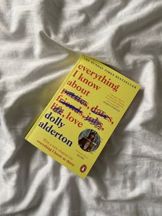 a yellow book sitting on top of a white sheet covered bed next to a pillow