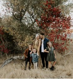 a family poses for a photo in front of a tree with red leaves on it