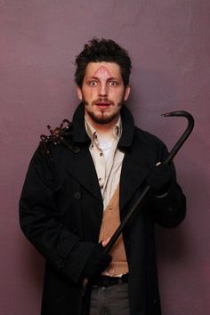 a man holding an umbrella and looking at the camera while standing against a purple wall