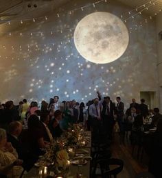 a large group of people standing in front of a full moon projected on the wall