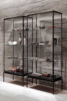 two glass shelves with shoes on them in front of a stone wall and flooring