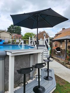 an outdoor bar with umbrellas and chairs next to a swimming pool in a backyard