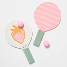 two ping pong paddles on a white surface with pink and green balls next to them