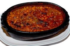 a white plate topped with a black casserole filled with beans and meats