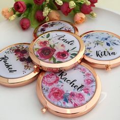 four personalized compact mirrors sitting on top of a white table with flowers in the background