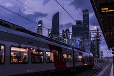 a train traveling down tracks next to tall buildings at night with lights in the windows