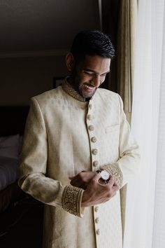 a man standing next to a window wearing a white suit and holding a cell phone