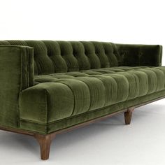 a green velvet couch with wooden legs on an isolated white flooring area, in front of a plain background