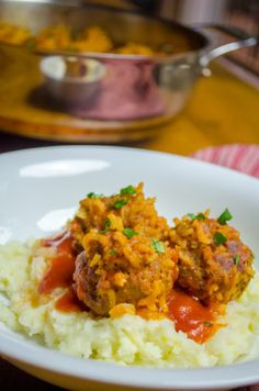 meatballs and mashed potatoes are served on a white plate with sauce in the background