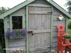 a small wooden shed with flowers in the window and a red chair next to it