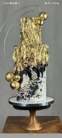 a white and black cake with gold decorations on it's top tier, sitting on a wooden table