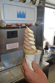 a person holding an ice cream cone in front of a machine with other items on it