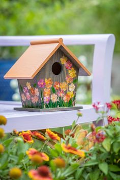 a bird house sitting on top of a white bench surrounded by flowers and greenery