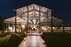 a group of people standing in front of a glass building at night with candles on the walkway