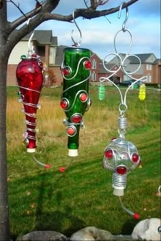 three glass ornaments hanging from a tree in front of a building with grass and rocks