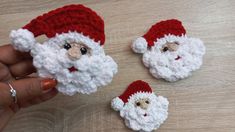 crocheted santa claus ornaments are being held by someone's hand on a table