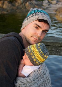 a man holding a baby wrapped in a knitted sweater and hat while posing for the camera