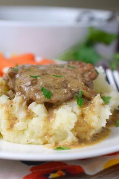 a white plate topped with mashed potatoes covered in gravy next to carrots