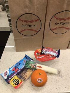 an orange sitting on top of a counter next to two bags with baseballs and candy