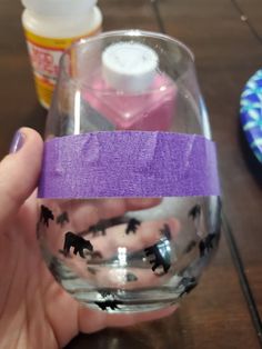 a hand holding a wine glass with purple tape around it and black cats on the inside