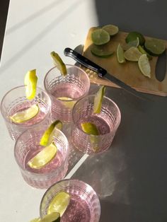 several glasses filled with lemonade and limes on a table next to a cutting board