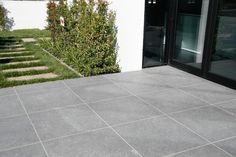 a concrete patio with steps leading to the front door and green bushes in the background