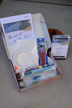 an open box with pens, paper and other items in it sitting on the ground