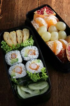 two black trays filled with sushi and fruit on top of a wooden table