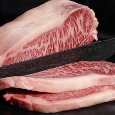 two pieces of raw meat next to a knife on a black surface with white and red patterns