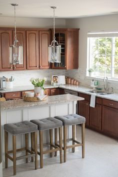 a kitchen with wooden cabinets and marble counter tops, three stools in front of the island