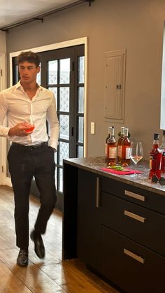 a man in a white shirt and black pants is holding a red drink while standing in a kitchen