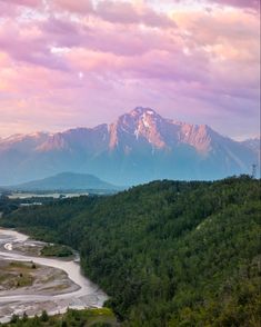 the mountains are covered in snow and green trees, with a river running between them