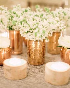 white flowers in gold vases on a table with candles and napkins around them