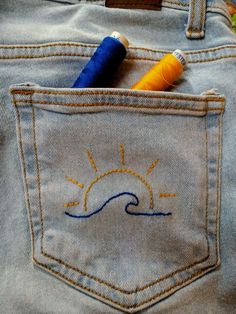 the back pocket of a pair of blue jeans with embroidered sun and ocean waves on it