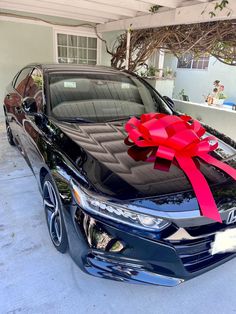 a black car with a red ribbon tied around it's hood in front of a house