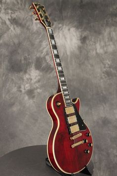 a red electric guitar sitting on top of a black stand in front of a gray background