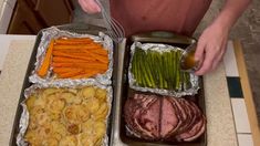 two trays filled with meat, potatoes and asparagus