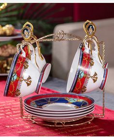 two teacups are being held over plates on a table with red and gold decorations