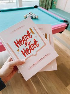 a person holding up two pamphlets with the words heart for hearts on them in front of a pool table